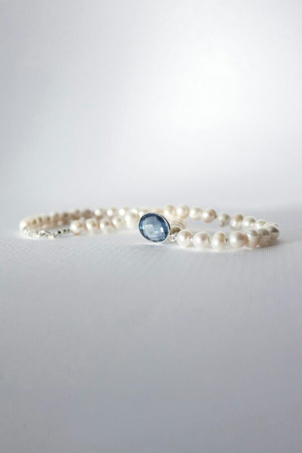 Close-up of an elegant pearl bracelet with a sapphire centerpiece on a soft background.