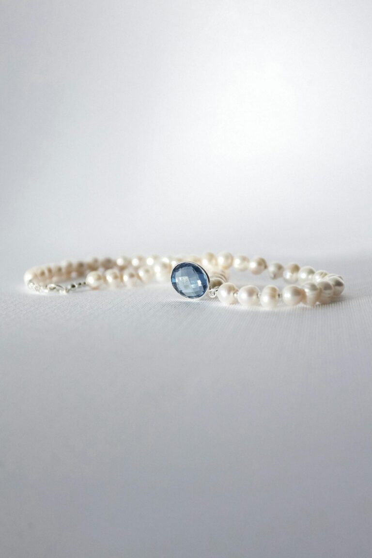 Close-up of an elegant pearl bracelet with a sapphire centerpiece on a soft background.