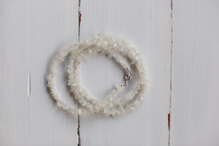 Simple white crystal bracelet with silver clasp on rustic white wood background.